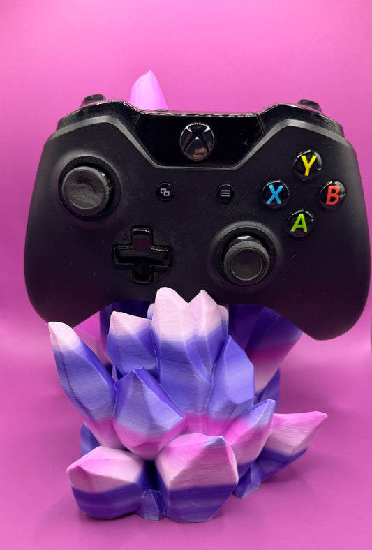 Black gaming controller on a pink and purple crystal stand against a pink background