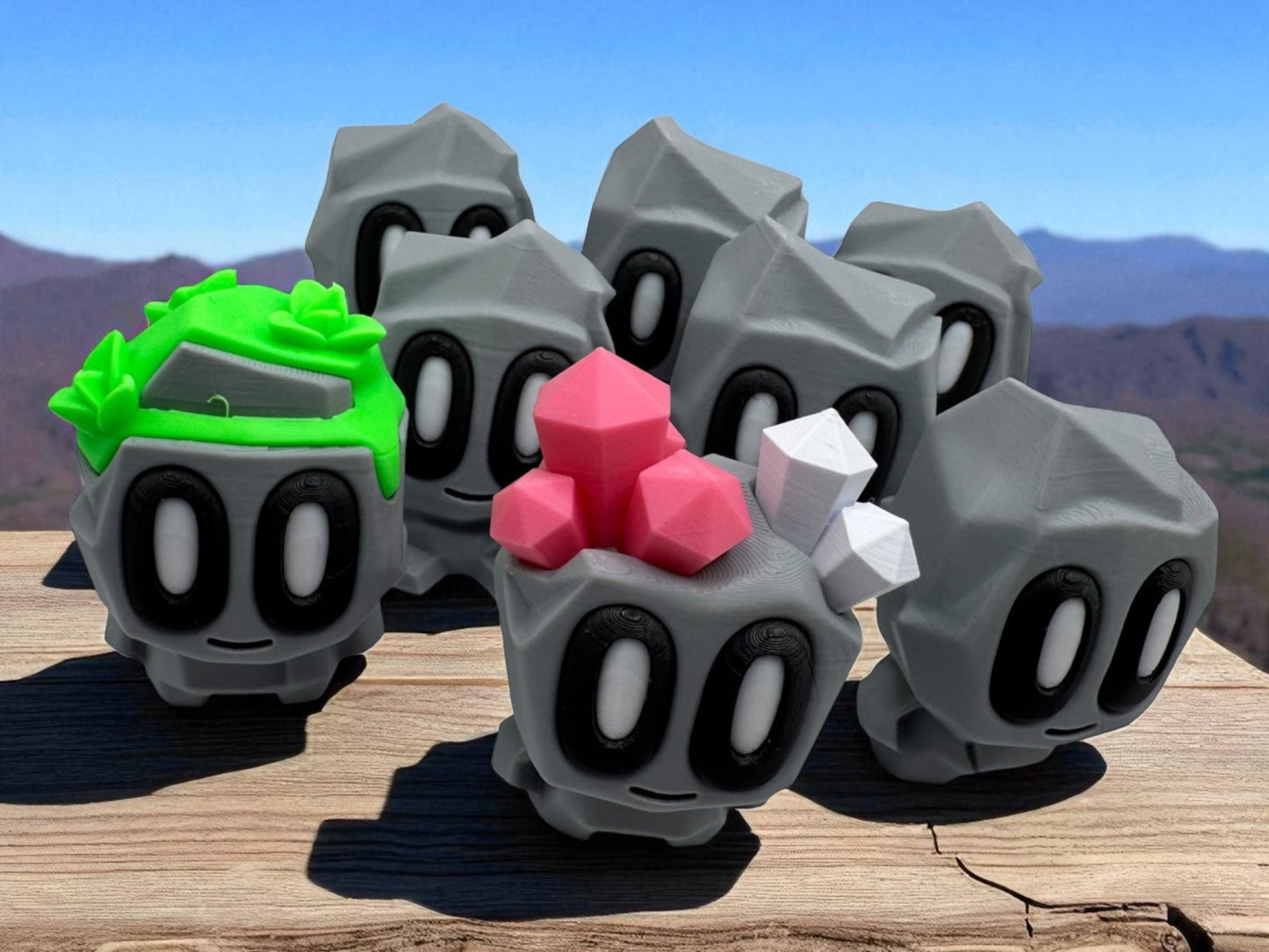 Gray stone-like figures with colorful tops on a wooden surface with a mountainous background